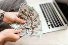 1600951323-close-up-woman-hands-holding-new-dollar-bills-she-earned-working-from-laptop-home-o...jpg